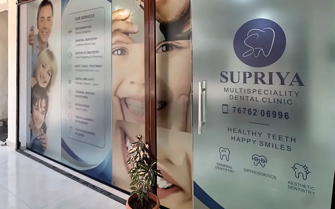 Glass entrance of Supriya Multispeciality Dental Clinic, showing the clinic name, phone number 76762 06996 and its services, on the 1st floor above Med Plus, Vidhya Nagar Circle