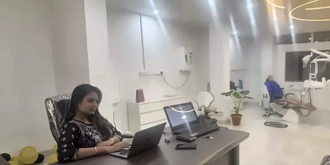 Dr. Supriya P working at her consultation desk, with the treatment area and its circular ceiling lights behind her