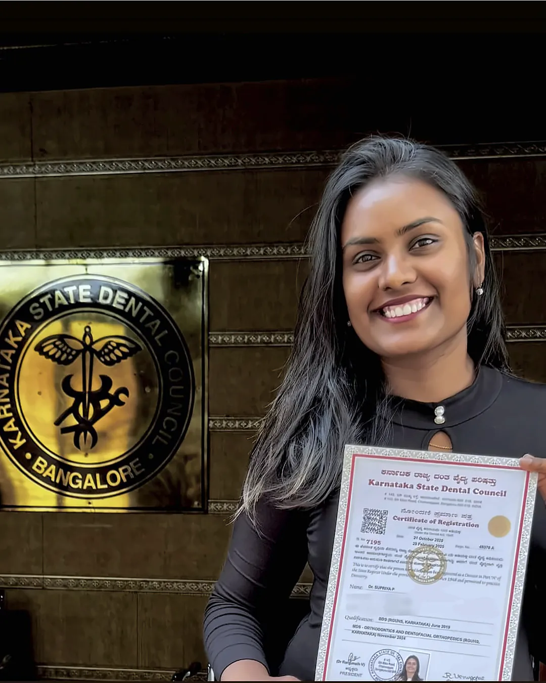 Dr. Supriya P holding her Certificate of Registration from the Karnataka State Dental Council, in front of the Council's emblem; personal details on the certificate are blurred